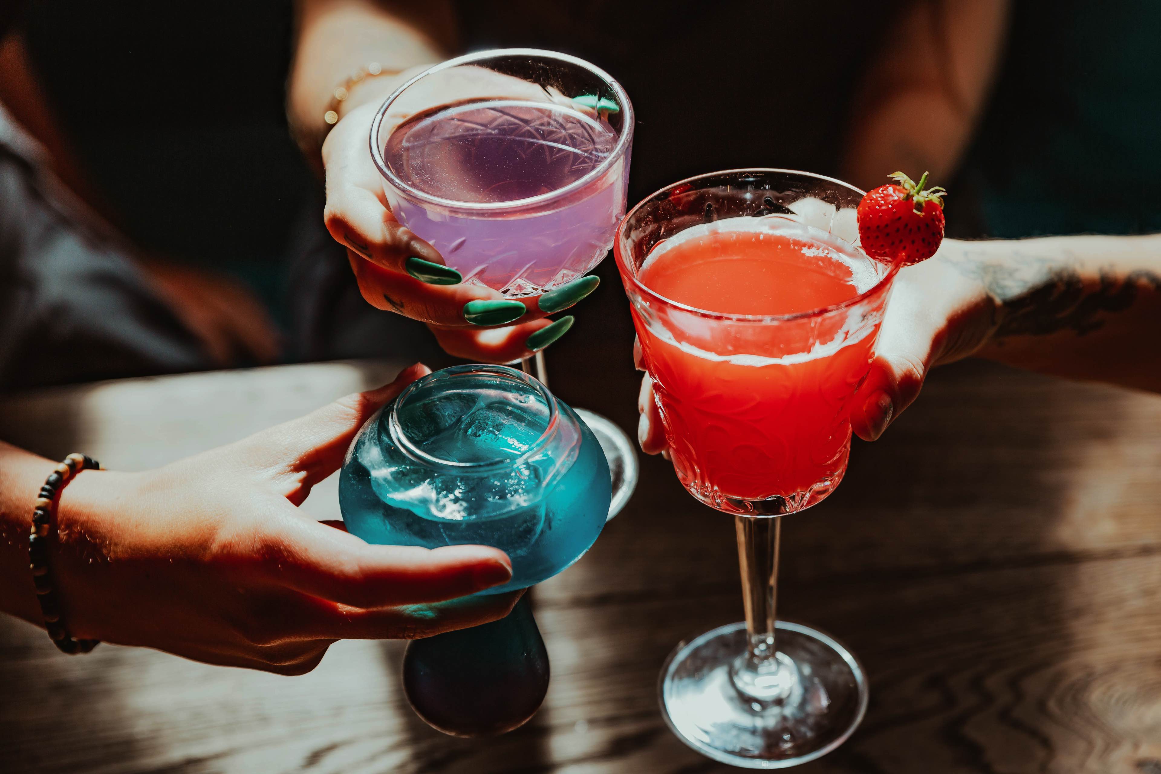 Three friends toasting three different brightly coloured cocktails